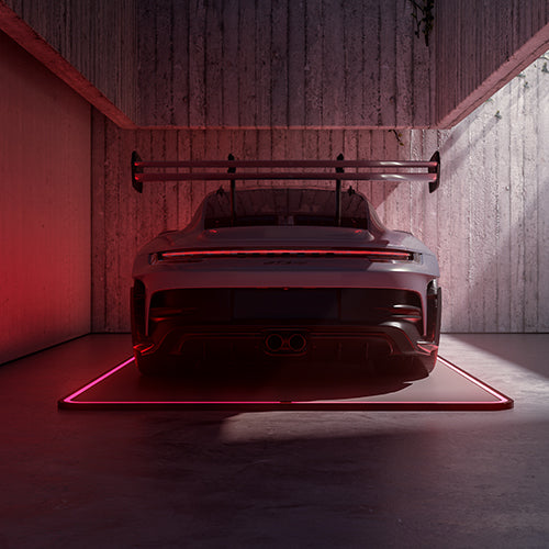 Sportwagen auf leuchtendem Pad in einer Holzgarage, von hinten bei schwachem rotem Licht gesehen.