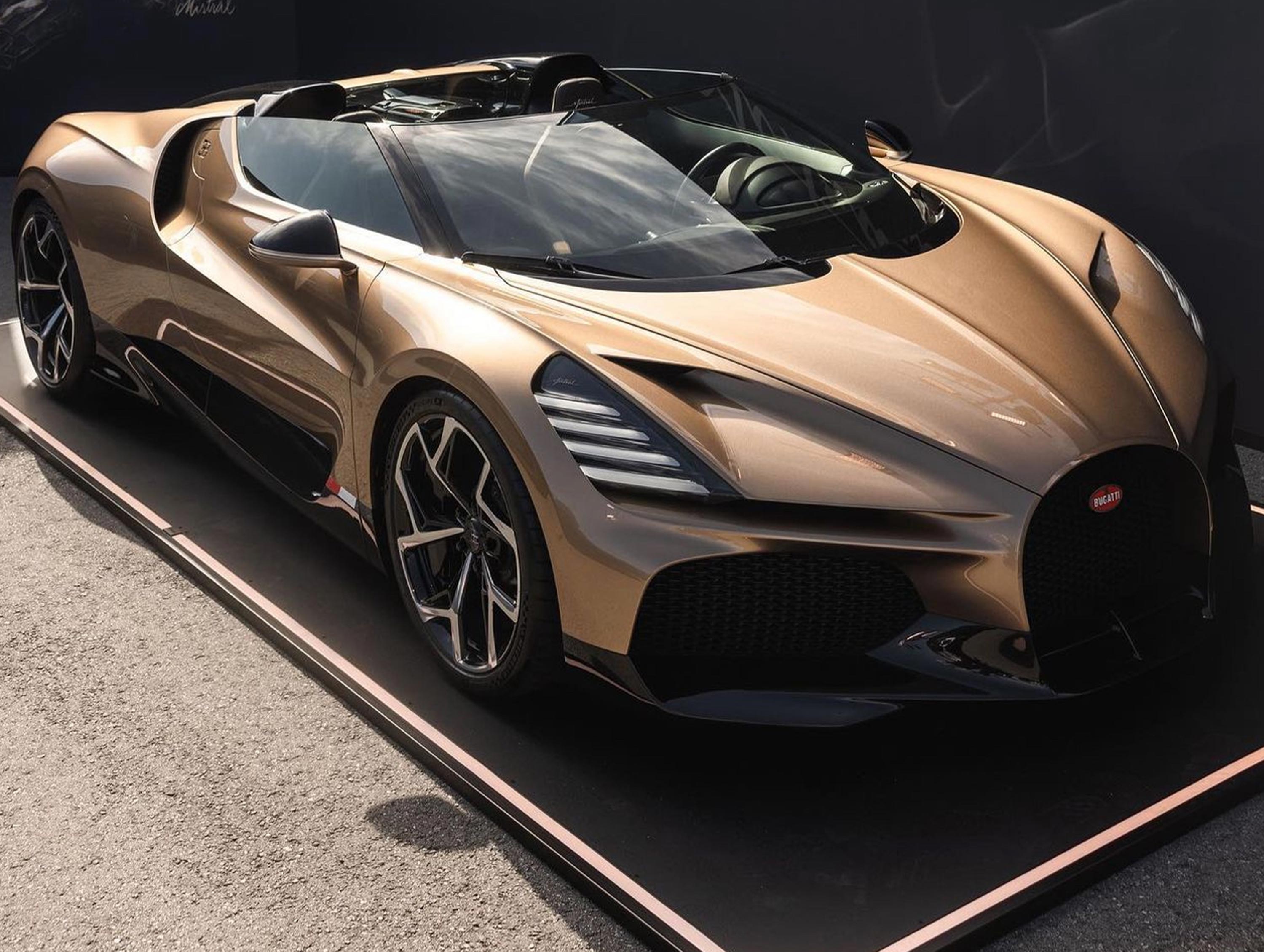 Goldener Sportwagen mit offenem Verdeck auf einem Ausstellungsplatz.