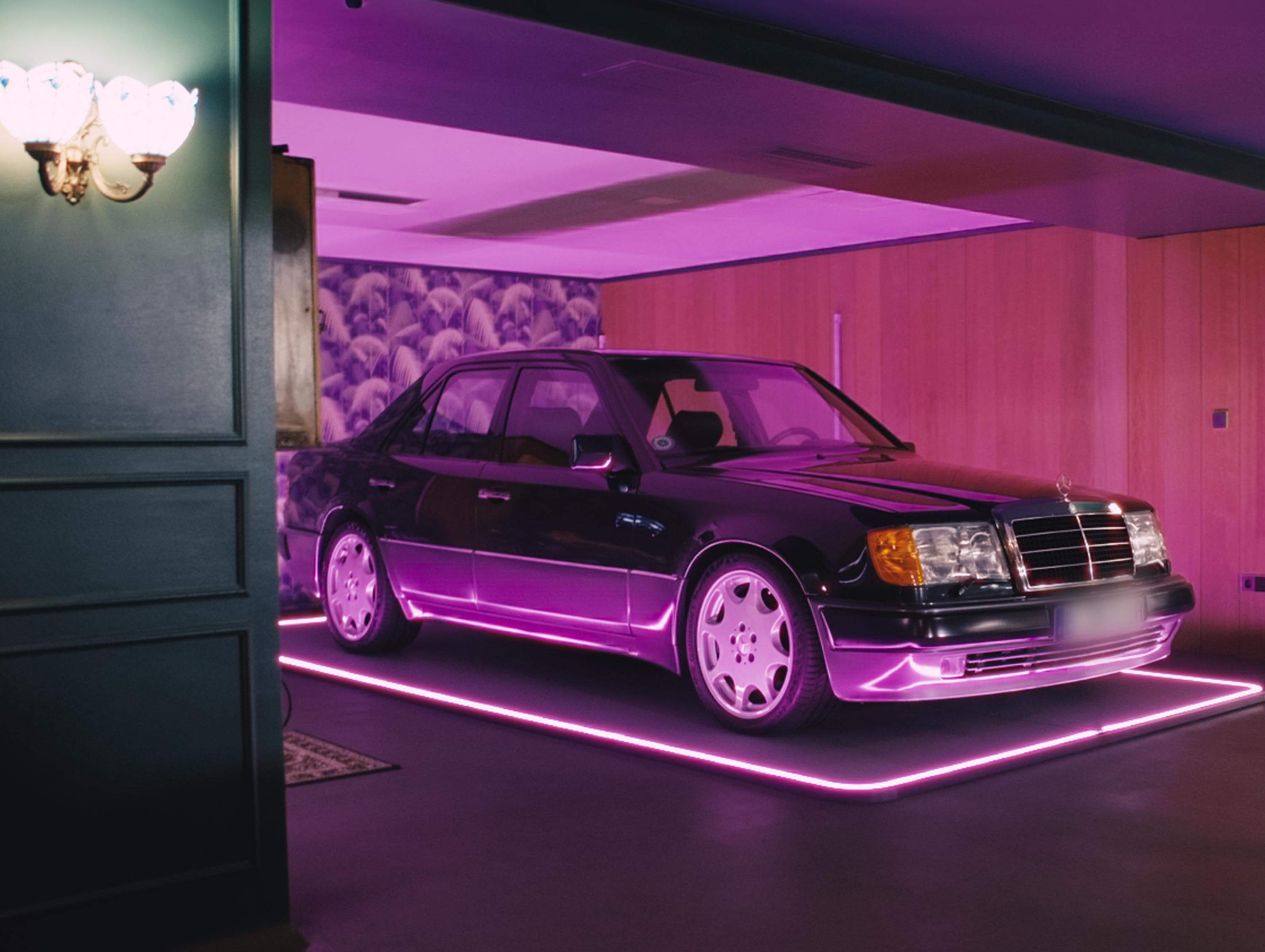 Auto auf beleuchtetem, rechteckigem Pad in einer Garage mit rosa Licht und floral gemusterter Wand.