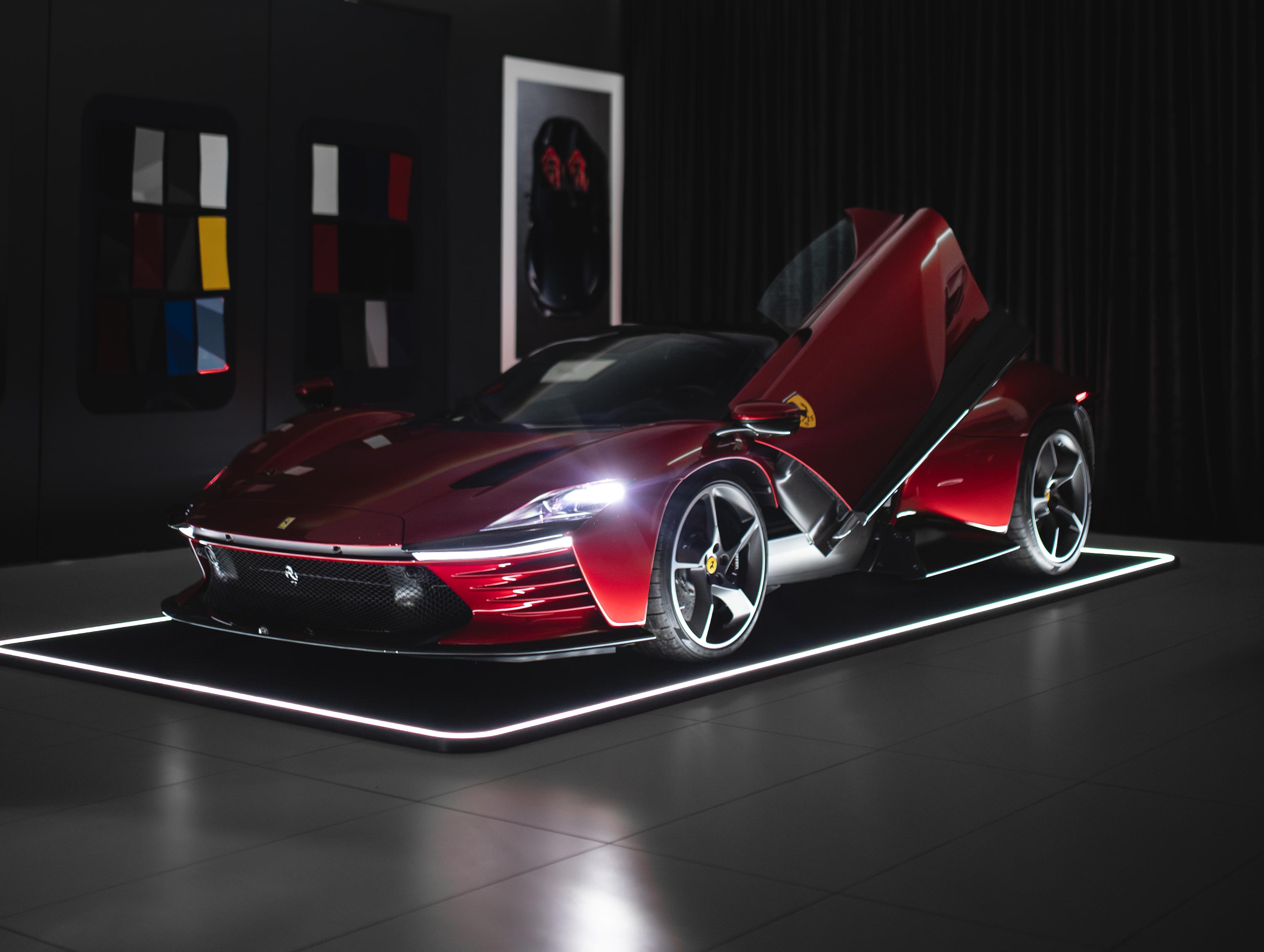 Ein rotes Sportauto mit Flügeltüren steht in einem beleuchteten Raum, umgeben von Farbmuster-Wänden.