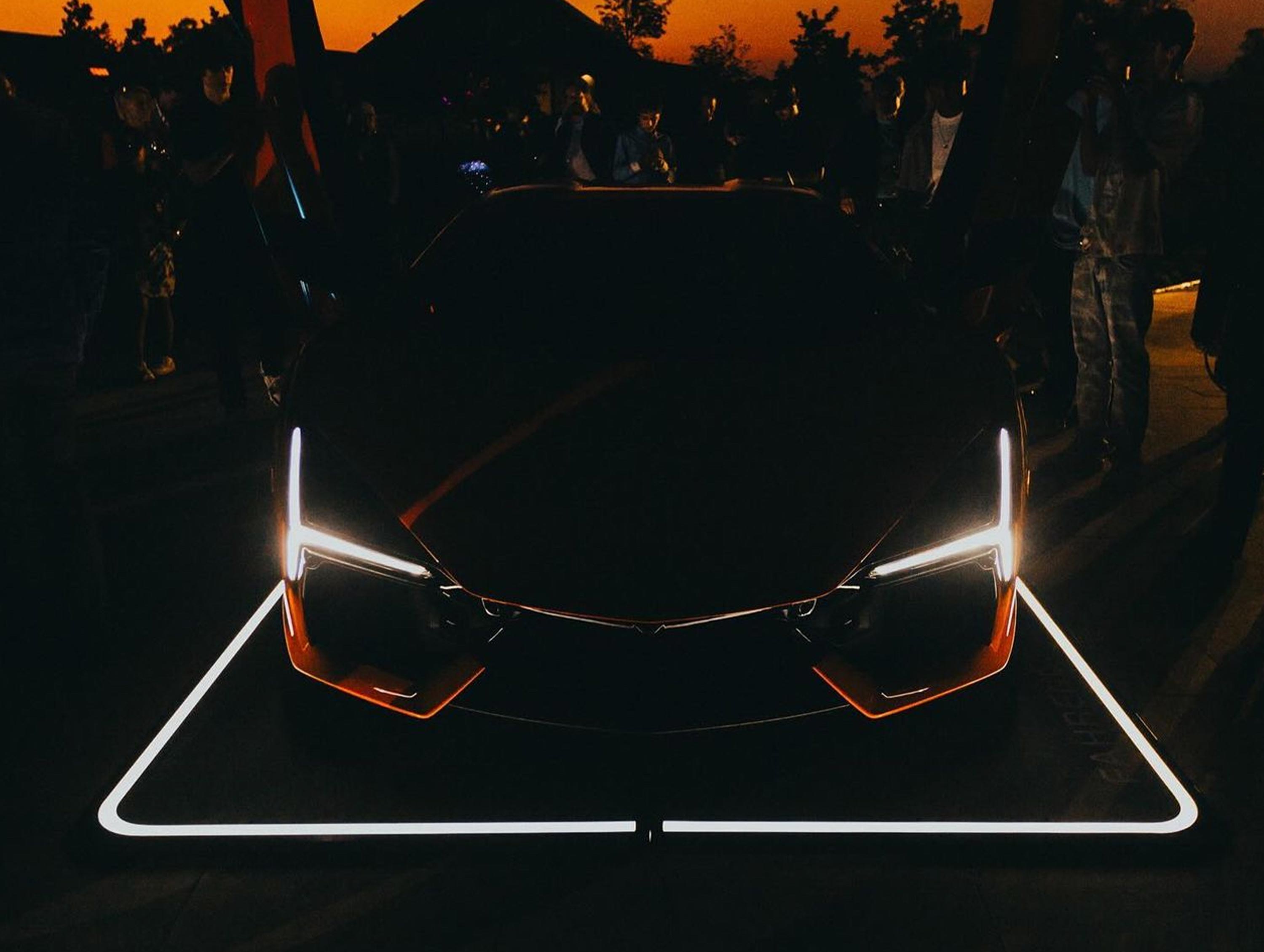 Sportwagen mit leuchtenden Scheinwerfern auf einem beleuchteten Fahrzeugpad, umgeben von Zuschauern in der Dämmerung.