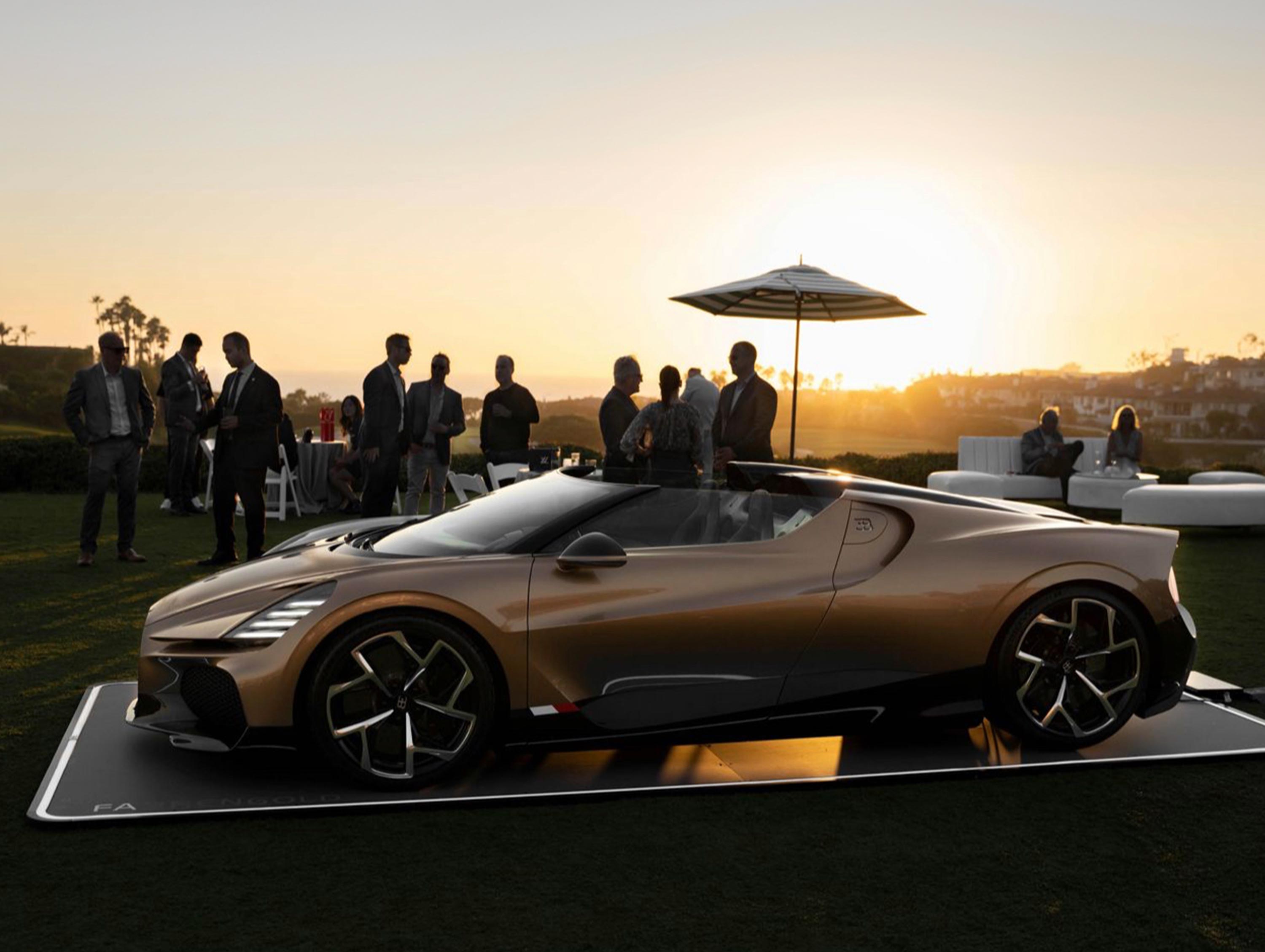 Ein Auto steht auf einem schwarzen Fahrzeugpad bei Sonnenuntergang, umgeben von Menschen und Sonnenschirm.