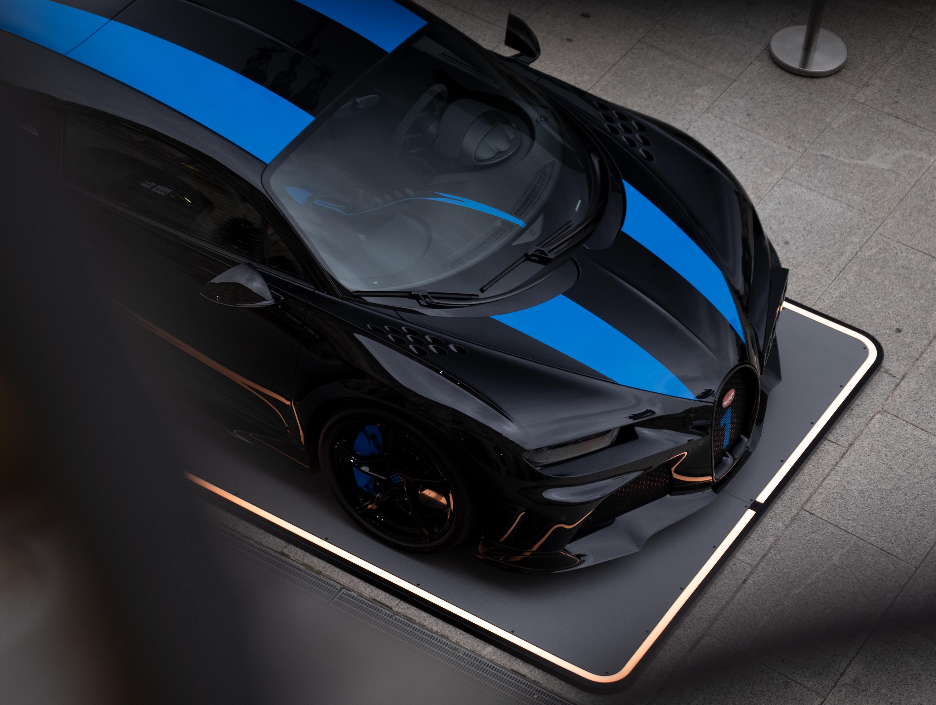 Schwarzes Auto mit blauen Streifen von oben auf einem rechteckigen Fahrzeugpad.