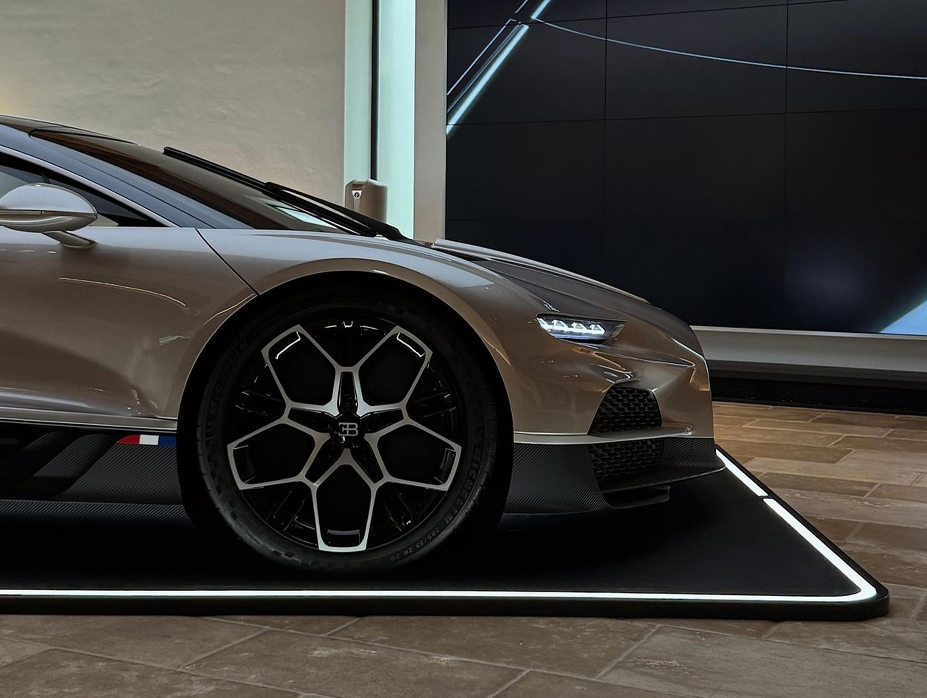 Ein luxuriöses Auto steht auf einem beleuchteten rechteckigen Pad in einem modernen Ausstellungsraum.