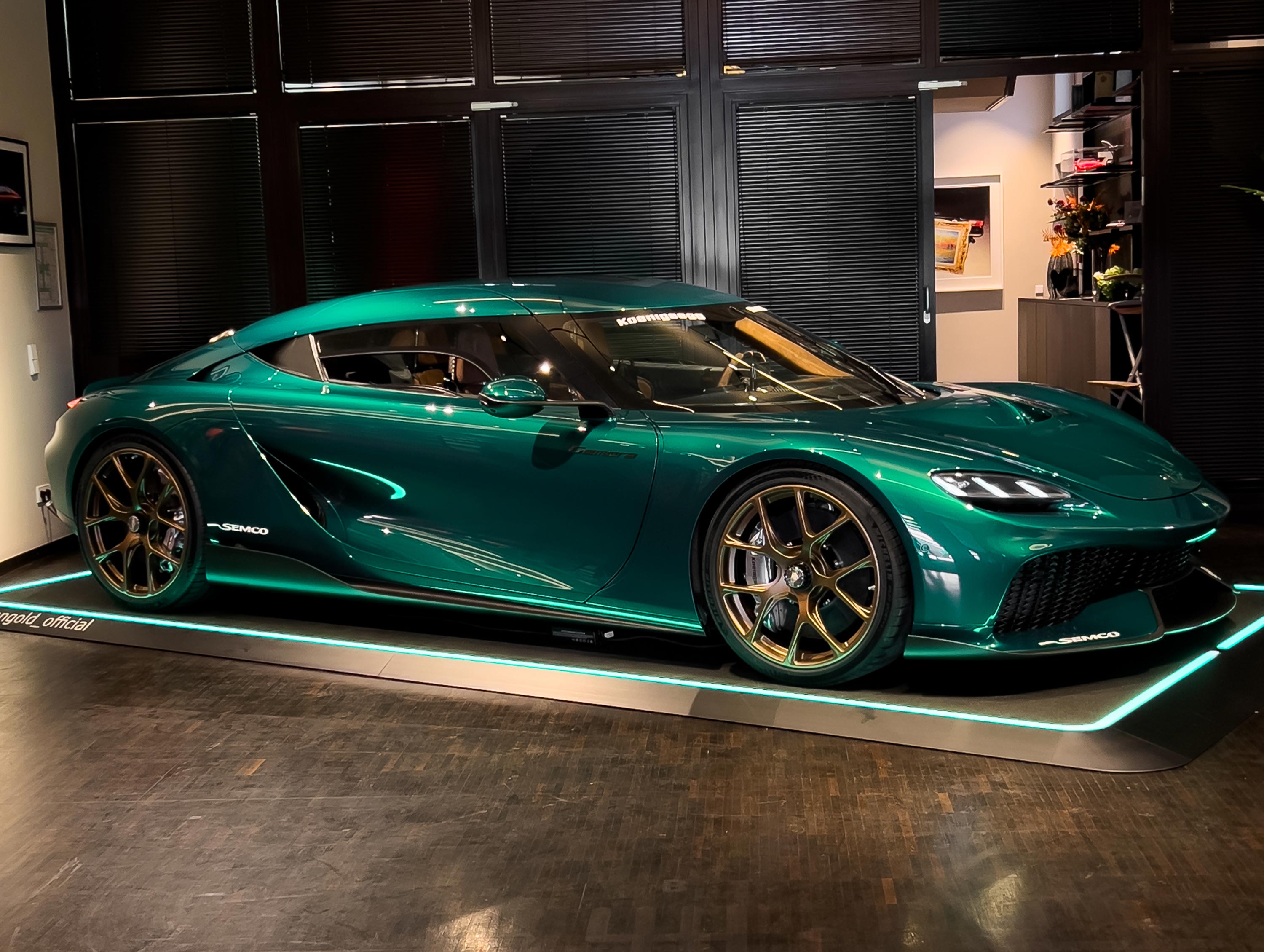 Grünes Sportauto mit goldenen Felgen auf einem Ausstellungsraum-Podest unter künstlichem Licht.