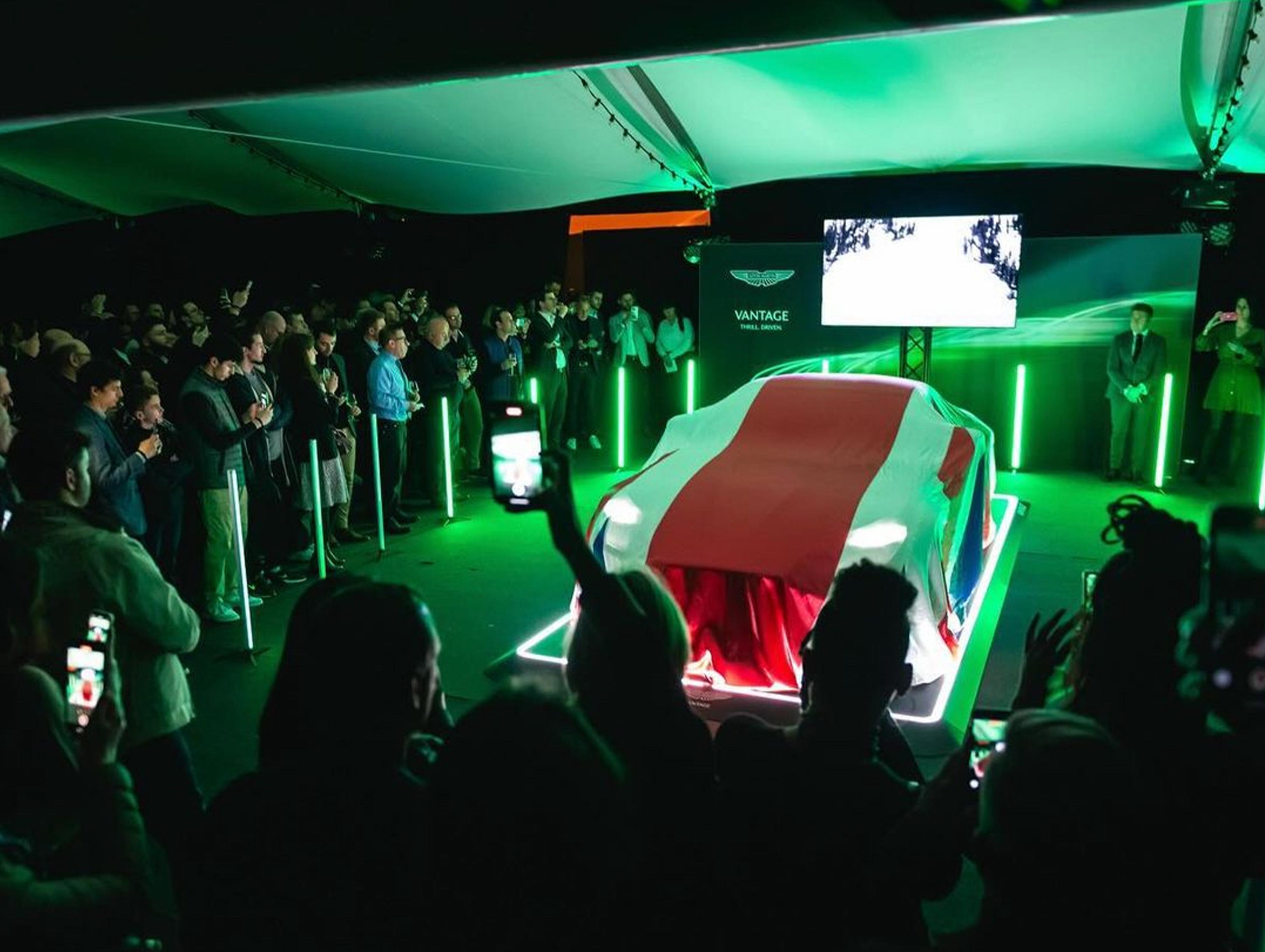 Menschen versammeln sich um ein mit einem Tuch bedecktes Auto bei einem Event unter grünem Licht.