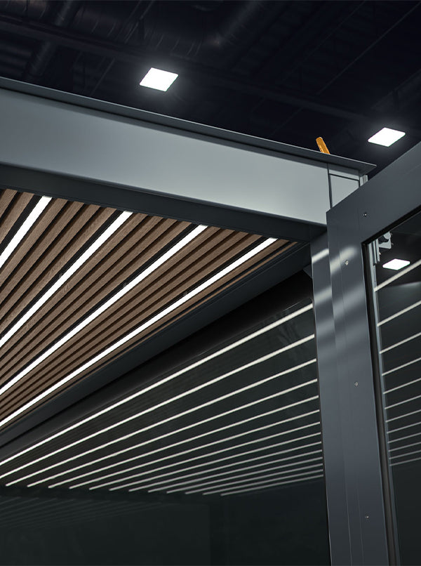 Riesige Lampe mit Holzleisten an der Decke eines modernen Gebäudes, hell erleuchtet in dunklem Raum.