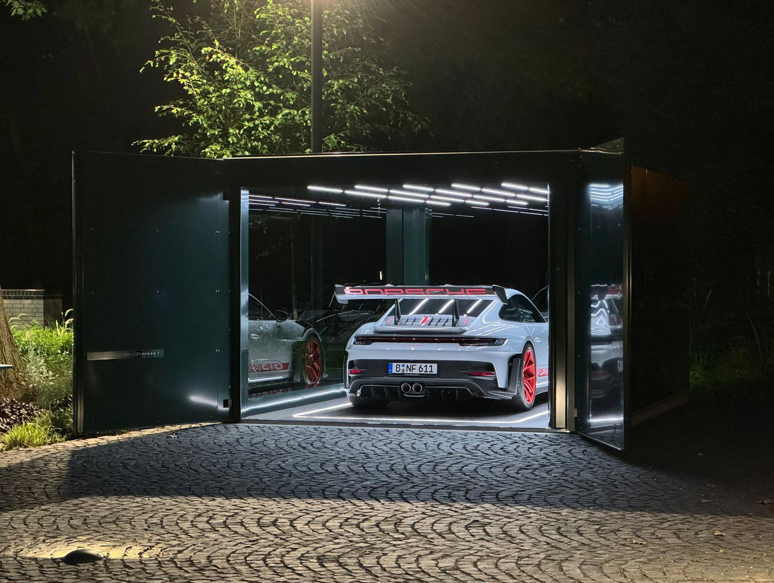 Ein weißes Auto mit rotem Spoiler und roten Felgen in einer beleuchteten Garage bei Nacht.