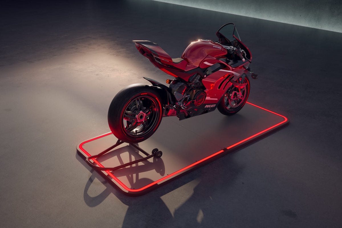 Rotes Motorrad auf einem beleuchteten rechteckigen Pad in einer dunklen Garage.