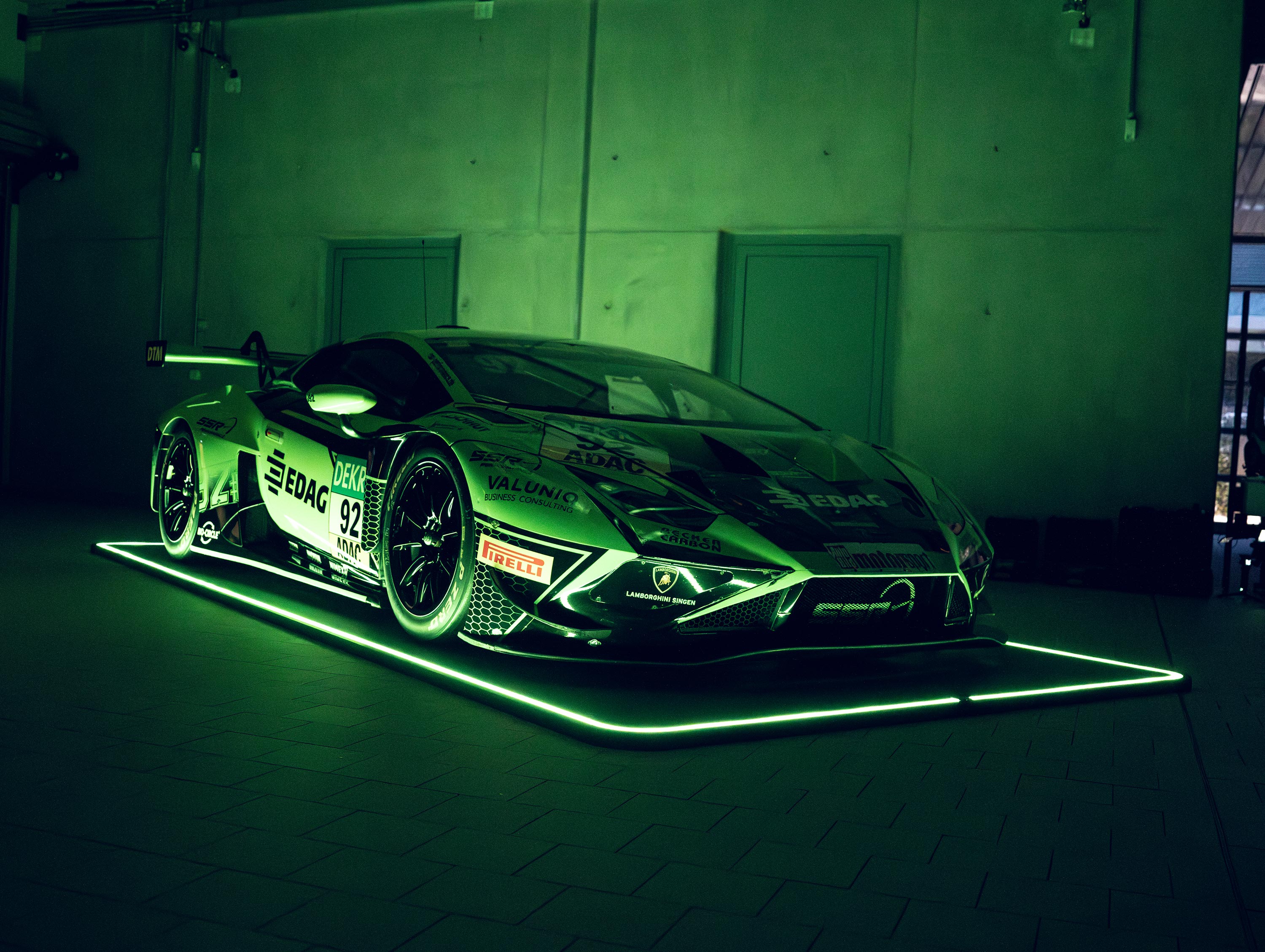 Rennwagen steht auf einem rechteckigen leuchtenden Pad in einer halbbeleuchteten Garage.