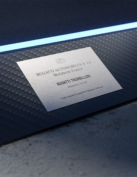 Metallplakette mit der Aufschrift "Bugatti Tourbillon" auf einer strukturierten Oberfläche unter blauem Licht.