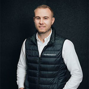 Ein Mann in weißem Hemd und schwarzer Weste steht vor einem dunklen Hintergrund.