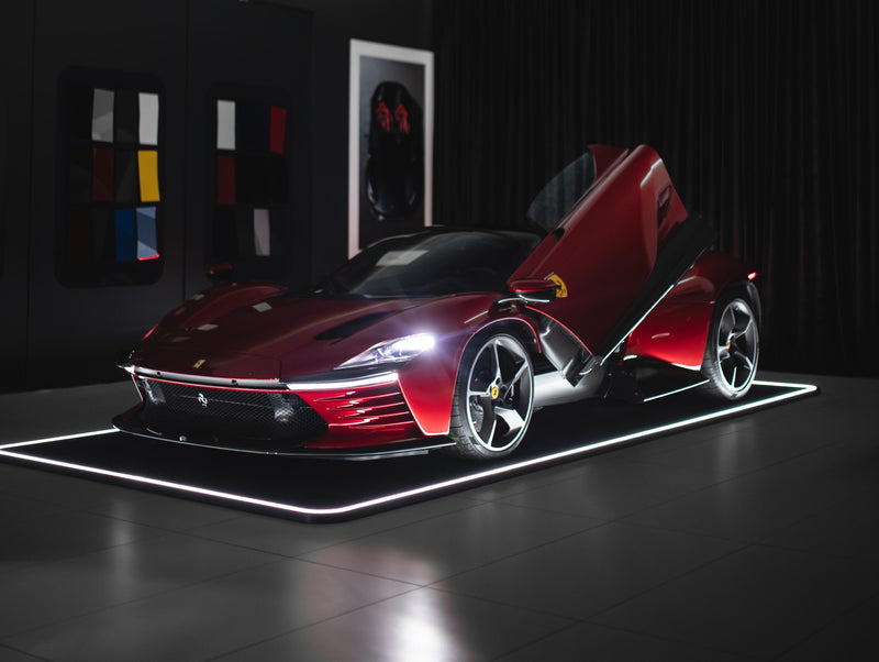 Ein rotes Sportauto mit Flügeltüren steht in einem beleuchteten Raum, umgeben von Farbmuster-Wänden.