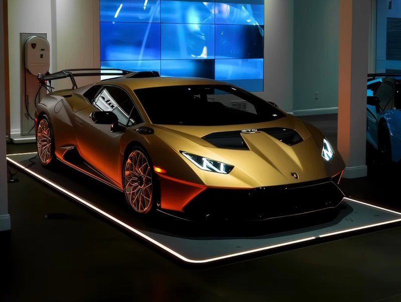 Goldener Sportwagen auf beleuchtetem Fahrzeug-Pad in einer modernen Garage, daneben ein Bildschirm und eine Ladestation.