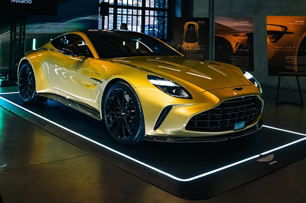 Gelbes Sportauto steht auf beleuchtetem Podest in einer Ausstellungshalle, umgeben von Informationsplakaten.