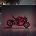Rotes Motorrad steht auf einem beleuchteten Boden, mit Palmen im Hintergrund bei Abenddämmerung.