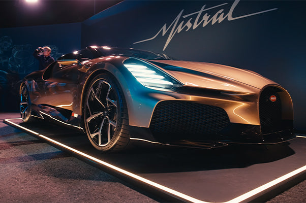 Sportwagen mit geschwungenem Design in einem Ausstellungsraum, begleitet von einem Fotografen im Hintergrund.